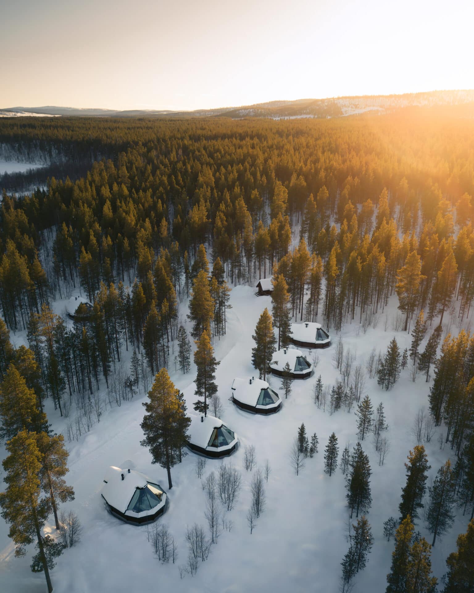 Aerial view of glass-roof cabins surrounded by snowy forest at Aurora Village Ivalo