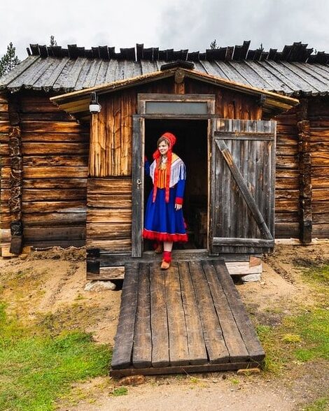 Traditional Sami hut in Lapland, Finland with a woman in colorful attire standing at the entrance.